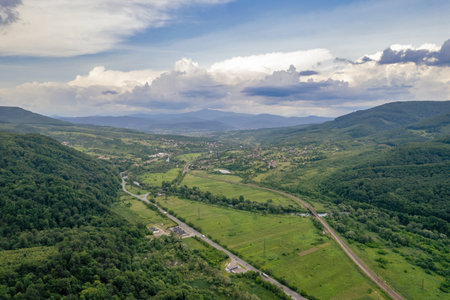 Scenic summer view of green forested hills and river Latorica valley with cloudy sky. Peaceful natural landscape ideal for travel, tourism, and nature backgrounds. Chynadiieve, Ukraine.の写真素材