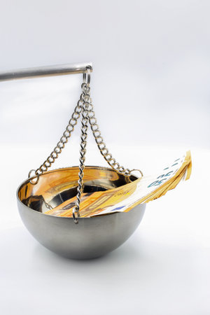 Stack of 50 euro currency banknotes placed in metallic hanging scale bowl with golden reflection, symbolizing financial balance, monetary weighing, economic justice and wealth measurement in business.の写真素材