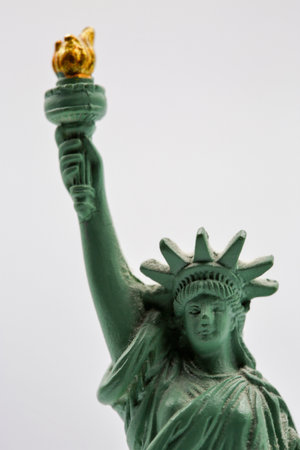 Small decorative Statue of Liberty replica figurine with green and gold patina finish, representing American icon, freedom symbol and New York City landmark souvenir collectible closeup on white.の写真素材