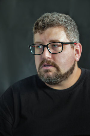 Studio portrait of young Caucasian man wearing glasses, reddish hair, beard and moustache on a black...