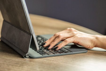 Closeup of thin woman hands typing on tablet keyboard at wooden desk. Modern mobile workspace,...