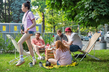 Kyiv, Ukraine - June 07, 2025: Group of friends relaxed on deck chairs at outdoor picnic at Food and Wine Festival. Wooden basket with gourmet food, wine glasses, and hot dogs. Social gathering.のeditorial素材