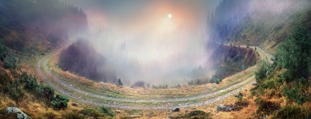 Amazing turn of the mountain road to the Transcarpathian mountain range. At the bottom of the gorge with streams, where clouds of thick fog, and the setting sun shines beautifullyの写真素材