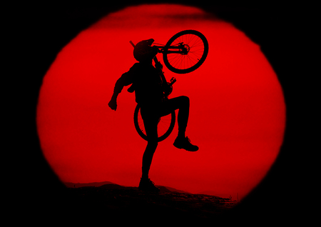 A cyclist travels through alpine hills and stands against a background of sunset with a mountain bike - MTB as a symbol. Extreme sports are dangerous in the mountains, and require high skill and trainingの写真素材