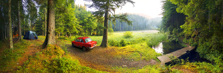 Ukraine, Verhovina- August 15, 2015: Fog after the rain covered mountain lake Ukrainian "Carpathian Eye" shore is covered with pine trees, where tent tourists and old Soviet car of local residents campersの写真素材
