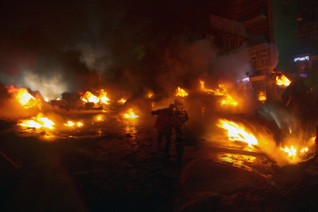 Kiev, Ukraine - January 22, 2014: Among the flame burning wheels rebel fighters try to contain the...
