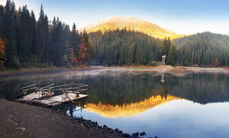 Autumn forest colorful over the water surface of a mountain lake, the largest in the Carpathian Mountains in the background. The famous pond attracts tourists  travelers to its shoresの写真素材