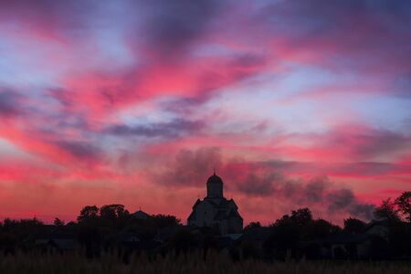 Under the sunset sky landscape of Ukrainian Orthodox Church in the village of ancient Ukrainian Carpathian on a hill near the ancient Galic on the background of flaming sunsetの写真素材