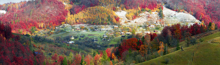 Cold autumn in Carpathian village. Bright colors after a snowfall blizzard is very beautiful scenic, beech, birch and pine forests and Hutsul houses on background ridge slopes Sokilskyの写真素材