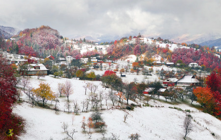 Cold autumn in Carpathian village. Bright colors after a snowfall blizzard is very beautiful scenic, beech, birch and pine forests and Hutsul houses on background ridge slopes Sokilskyの写真素材