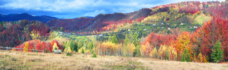 Cold autumn in Carpathian village. Bright colors after a snowfall blizzard is very beautiful scenic, beech, birch and pine forests and Hutsul houses on background ridge slopes Sokilskyの写真素材