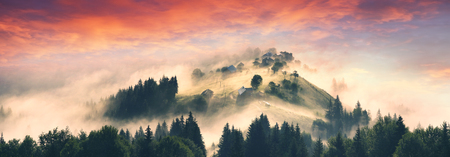 dawn in the mountains is fabulous and beautiful, the waves of the misty sea float in the valley against the background of high peaks covered with forests. At the bottom of the mountain villageの写真素材