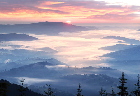 Western Europe mountainous terrain and alpine villages against the backdrop of the ridges bathe in the sea of fog after the rain on a warm summer morning at dawn in the pink raysの写真素材