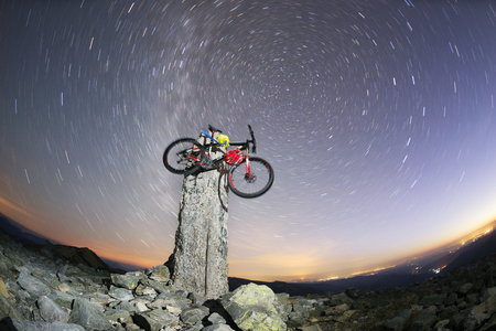 Placers with stones on a steep peak with a stone pillar, a mountain professional bicycle against the background of the Milky Way, the legendary summit of Mount Syvul in Gorgan in Ukraineの写真素材