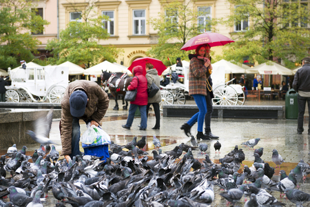 Poland, Krakow, September 14, 2015: Guests of the city, tourists and travelers, the townspeople feed a lot of hand-held pigeons on the ancient Market Square, the main sight of the cityのeditorial素材