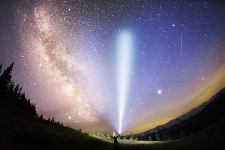 The dark mountain night shines with millions of stars over the fabulous Alpine peak in the Carpathians, the Milky Way of the Galaxy passes over a coniferous forest with a huge arcの写真素材