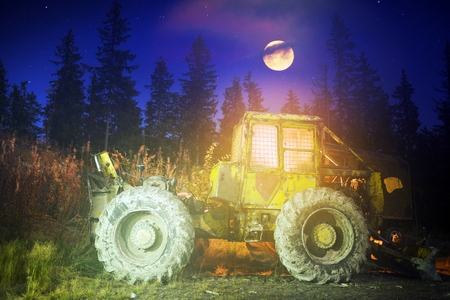 An ancient tractor at the top of the mountain for transportation of coniferous forest is illuminated by a photographer of various lights in the moonlit night in the Carpathians as an art objectの写真素材