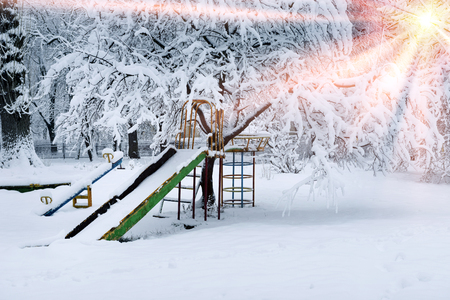 After a heavy snowfall, the fabulous beauty of the morning winter old park in Europe, Ukraine among the beautiful white trees are carousels, slides, attractions for children and parentsの写真素材