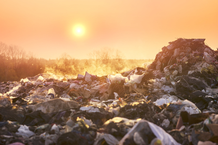 Sunrise on a huge trash can after a fire. Smoke and steam, poisonous gases and fumes escape from the waste of the city in the sunlight of dawn, harm the environmentのeditorial素材