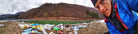 Ukraine, Kolochava, March 21, 2019: A tourist photographed with a mobile phone Xiaomi a panorama of ecological disaster - the river carries plastic waste to Europeのeditorial素材