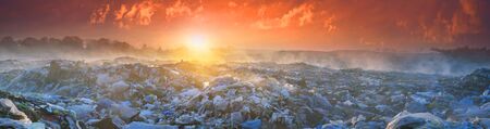beautiful foggy dawn of the Sun over a huge field of urban garbage, saturated with poisonous fumes of decomposition of organic waste and household chemicalsの写真素材