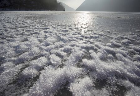 Mountain wild alpine lake surrounded by forest peaks shackled by severe frost, covered with snow...
