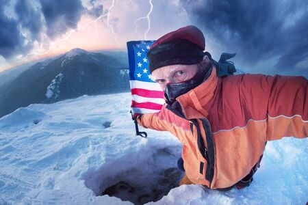 Snowy frosty peak with beautiful scenery at sunset mountain range in extreme frosty weather with an American climber in modern climbing equipment in a snow cave with the US flagの写真素材