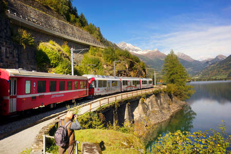 Switzerland, Poschiavo, October 10, 2019: Railroad train on the shore of Lake Poschiavo against the backdrop of alpine peaks. It connects the cities of St. Moritz in the canton of Graubunden, Switzerland and Tirano, in the province of Sondrio, Italy, throのeditorial素材
