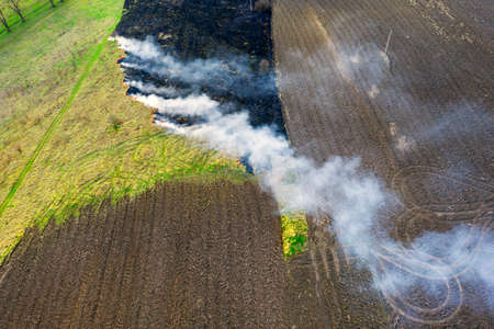 setting fire to the grass in spring. Poisonous dangerous smoke, death of animals, plants, birds and insects, aerial photos, drone. Contrast between the green of the field, arable land and a burnt placeの写真素材