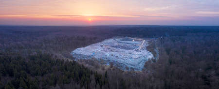 A bright red sunrise over a large wild forest in which the city's trash can is a landfill for...