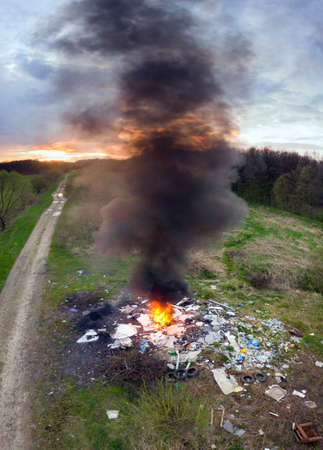 Car tires are burning in an illegal spontaneous garbage dump outside the city, poisoning the atmosphere with poisonous emissions of gases and aerosols of smoke. View from a drone copterの写真素材