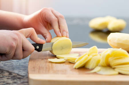 Cropped close up shot of a woman cutting up potatoes on a cutting board.Concept of preparing an traditional spanish omeletteの写真素材