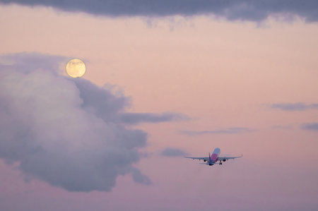 a departing plane at night, against the backdrop of a full moon, sets off on its evening flightの写真素材