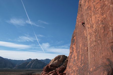 wide angle view of a rock climber in red climbing a tall red sandstone cliff at Red Rocks, Nevadaの写真素材