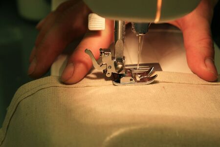 close up of sewing machine sewing tan canvas cloth held by a man's hand