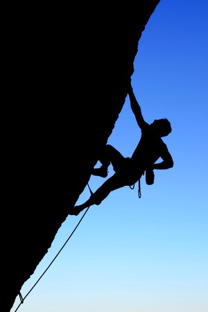 silhouette of rock climber climbing an overhanging cliff with blue sky backgroundの写真素材
