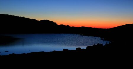 before sunrise the sky turns reddish over an alpine lakeの写真素材