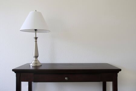 silver table lamp sitting on a wooden table with a white wall in the background and copy spaceの写真素材
