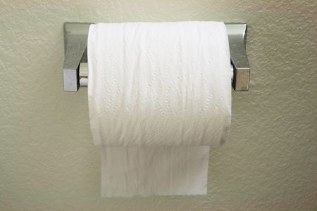 a toilet paper roll dispenser with the paper feeding over the top towards the backの写真素材