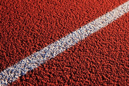 detail of diagonal white line on a red rubber track surfaceの写真素材