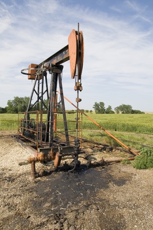 orange and black rusty oil well pump in a fieldの写真素材