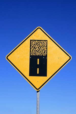 gravel road sign warning of a change from paved to unpaved road surface with blue sky backgroundの写真素材