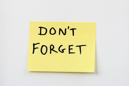 don't forget on a small yellow sticky note stuck on a white wallの写真素材