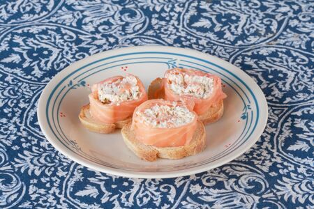 smoked salmon rolled around cheese and herb filling on toasted french bread appetizers on a plateの写真素材