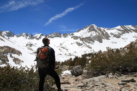 the back side of a male backpacker looking at snowy sierra mountains