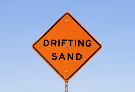 orange and black drifting sand road sign with blue sky background