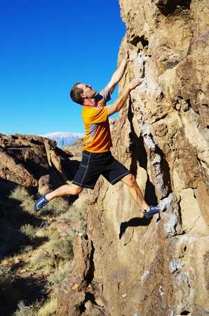 side view of man in an orange shirt rock climbing a boulderの写真素材