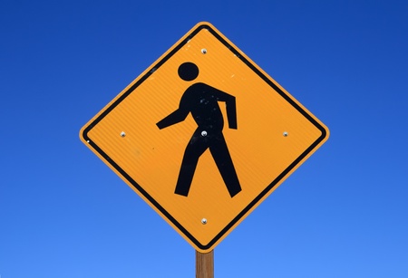 pedestrian sign with a person walking on yellow with a blue sky backgroundの写真素材
