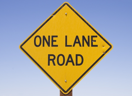 yellow and black one lane road sign with blue sky backgroundの写真素材