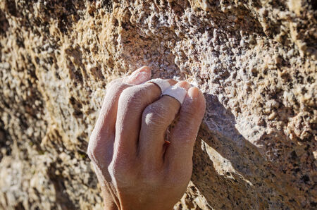 the hand of a woman climber in a crimp grip grabbing a small granite rock climbing holdの写真素材